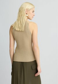 Top in maglia beige con design aderente, caratterizzato da spalline sottili. Abbinato a una lunga gonna verde oliva e orecchini dorati.