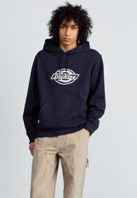 Hoodie bleu marine en tissu coton mélangé, doté d'une poche avant et d'un logo circulaire avec le texte "Dickies" en blanc.