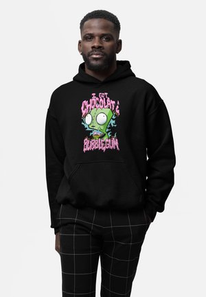 Mann trägt schwarzen Hoodie mit grünem Cartoon-Charakter und buntem Schriftzug „I got chocolate bubblegum“, kombiniert mit schwarzen karierten Hosen.