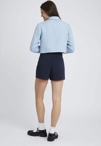 Veste courte texturée bleu clair, shorts marine et chaussures à plateforme noires avec des chaussettes blanches jusqu'aux chevilles. Design simple avec un col.