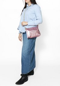 Borsa a tracolla metallica rosa con finitura testurizzata e design geometrico. Abbinata a una camicia azzurra chiara e una gonna di jeans, che mostra uno stile casual.