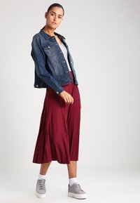 Jeansjakke med en tettsittende design, lys blå farge; kombinert med en flytende burgunder plisserte skjørt og grå sneakers med hvite detaljer.
