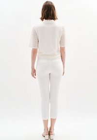 Witte, textuurgevestigde top met korte mouwen en kraag, gecombineerd met witte, aansluitende broek tot de enkel en sandalen, gezien vanaf de achterkant.