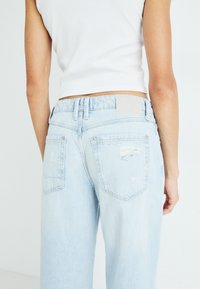 Ανοιχτό μπλε τζιν παντελόνι με φαρδιά γραμμή, διαθέτει φθαρμένα σημεία, ορατές ραφές και πίσω τσέπες. Ουδέτερη ετικέτα στη ζώνη.