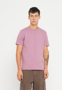 Kortærmet t-shirt i lys mauve bomuld med crew neck og en glat tekstur. Parret med mørkebrune cargo bukser.