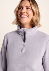 Light purple fleece pullover with a short zippered collar, featuring a contrasting black zipper and soft texture.