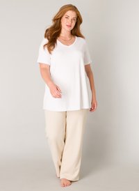 Witte T-shirt met korte mouwen en V-hals, gecombineerd met losse beige broek. De stof lijkt glad en lichtgewicht, met een relaxed fit.