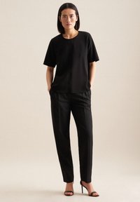Top nero a maniche corte con scollatura rotonda, abbinato a pantaloni neri su misura con taglio dritto, completato da eleganti tacchi alti neri.