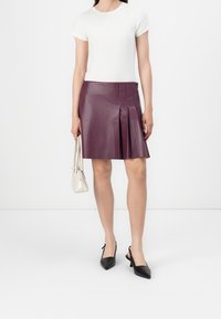 Kožená plisovaná mini sukně v tmavě fialové barvě, zkombinovaná s přiléhavým bílým tričkem. Doplněno malou krémovou kabelkou a černými podpatky.