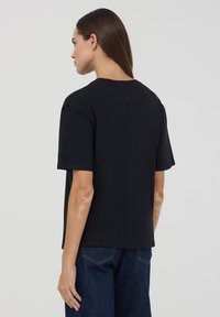 Czarny t-shirt z krótkim rękawem i okrągłym dekoltem, wykonany z bawełny. Charakteryzuje się luźnym krojem i prostym designem, bez widocznych logo czy wzorów.