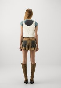 Háčkovaný top v krémové barvě spárovaný s hnědou džínsovou sukní s rozšířeným lemem. Kozačky hnědé barvy z kůže do výšky kolen s mírným podpatkem.