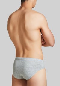 Slip grigio in cotone con una superficie liscia, design a vita bassa e senza cuciture visibili, visti da dietro. Presenta una silhouette minimalista.