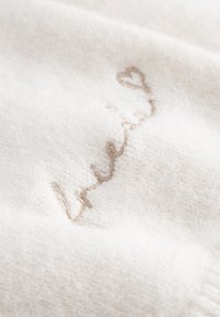 Crèmekleurige stoffen met zachte vezels, met delicate beige geborduurde tekst en een klein hartontwerp.