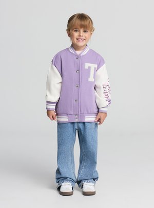 Giacca varsity color lavanda con maniche bianche, bottoni frontali e logo; abbinata a jeans a gamba larga azzurri e sneakers bianche.