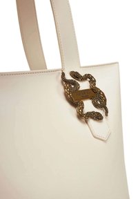 Borsa tote in pelle crema con un accentuato hardware a forma di serpente in tono oro e un'etichetta esagonale in pelle. Texture liscia, silhouette semplice.