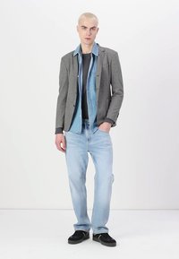 Grau, Blazer über einem Jeanshemd, kombiniert mit einem dunklen T-Shirt und hellblauen Jeans. Schwarze Sneaker runden das Outfit ab. Glatte Texturen und Schichtdesign.