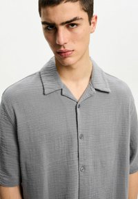 Gray short-sleeve shirt made of textured fabric, featuring a camp collar and button-down front. Soft texture with a relaxed fit.