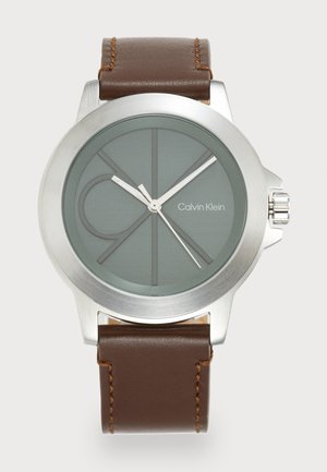 Orologio in acciaio inossidabile argento con quadrante verde, cinturino in pelle marrone e accenti argentati. Presenta un design minimalista con logo e indici strutturati.