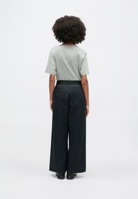 T-shirt cinza de manga curta combinada com calças pretas largas com cós elástico. O conjunto é simples e funcional, sem padrões visíveis.