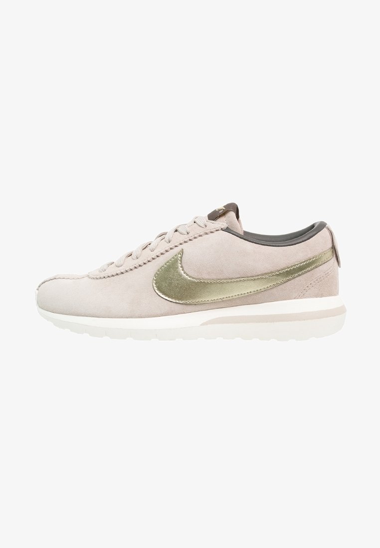 Vaaliharmaat mokkanahkakengät, joissa on metallinhohtoinen kultainen swoosh, pyöreä kärki ja valkoinen kumipohja. Korissa ja nauhoissa on harmaita yksityiskohtia.