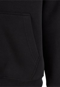 Gros plan sur la poche d'un sweat à capuche en tissu noir avec des coutures visibles et un ourlet côtelé en bas.