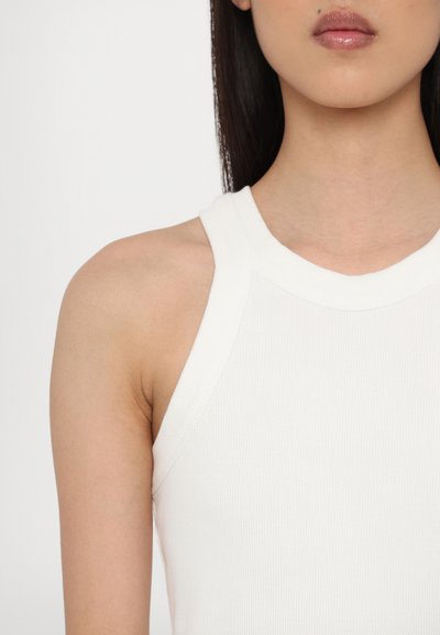 Weißes, geripptes Tanktop mit hohem Halsausschnitt und breiten Trägern, das eine taillierte Silhouette und strukturierten Stoff aufweist.
