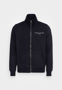 Chaqueta negra de cremallera completa con cuello alto, bolsillos frontales y logo "Tommy Hilfiger EST. 1985" en el pecho, además de un pequeño logo en el puño izquierdo.