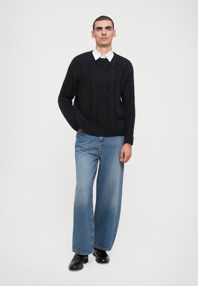 Black cable-knit sweater with a round neck, paired with light blue wide-leg denim jeans. Black shoes complete the outfit.