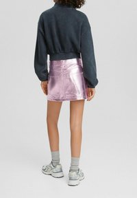 Avskuren mörkgrå sweatshirt med långa ärmar i kombination med en glänsande rosa minikjol, som har bakfickor och en blank yta. Bärs med grå strumpor och sneakers.