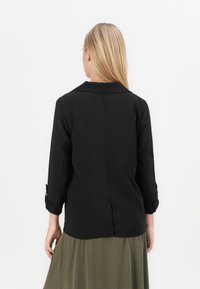 Czarna bluzka z kołnierzykiem i rękawami o długości trzy czwarte, z zawiniętymi mankietami i rozcięciem z tyłu. Gładki materiał, minimalistyczny design.