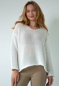 Biały sweter z dzianiny o luźnym kroju i dekolcie w serek, charakteryzujący się otwartą strukturą splotu i lekko oversize'owymi rękawami. Zdobiony prążkowanym wykończeniem.