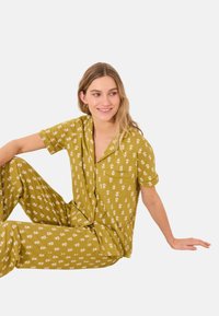 Gelbes, blumig gemustertes Loungewear-Set mit lockerem Schnitt, kurzen Ärmeln und einer Tasche auf dem Shirt. Weicher Stoff, locker sitzende Hose.