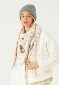 Gray ribbed knit beanie and a cream scarf with a pink and brown geometric pattern, draped loosely over a white jacket and beige knit top.