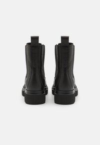 Stivaletti neri in pelle con una finitura testurizzata, punta arrotondata e suola in gomma spessa. Presentano delle linguette sul retro per una facile calzata.