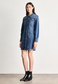 Μπλε τζιν φόρεμα πουκαμίσου, με δύο τσέπες στο στήθος, κουμπιά μπροστά, μακριά μανίκια και λίγο ξεφτισμένο στρίφωμα. Συμπληρώνονται από μαύρες μπαλαρίνες ankle.