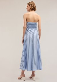 Rochie albastră fără bretele, cu dungi verticale, spate elastificat și hem fluid. Material ușor, lungime până la jumătatea gambei, asortată cu sandale cu talpă înaltă.