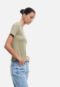 Olijfgroen t-shirt met korte mouwen en een gestructureerd oppervlak, gecombineerd met lichtblauwe, ruime jeans. Eenvoudig en casual ontwerp.