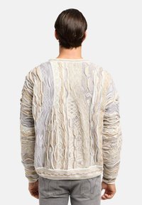 Textuurtweater in beige en grijs met ingewikkelde patronen en gelaagde ontwerpen. Aansluitende manchetten en zoom met een relaxed fit, die unieke details toont.