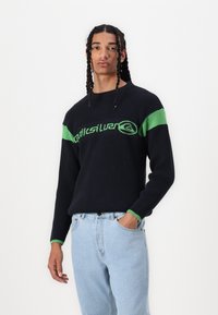 Pulover navy cu dungi verzi și logo pe piept. Material ușor, guler rotund și croială relaxată. Purtați cu blugi albastri deschiși.