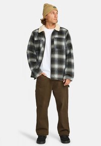Plaid flannel shirt in dark blue, gray, and white; faux fur collar; worn over a white T-shirt; brown pants; black shoes; casual fit.
