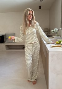 Conjunto de loungewear a rayas, en tonos beige claro y crema, que incluye una camiseta de manga larga y pantalones con cordón, fabricado en tejido suave y con un corte holgado.