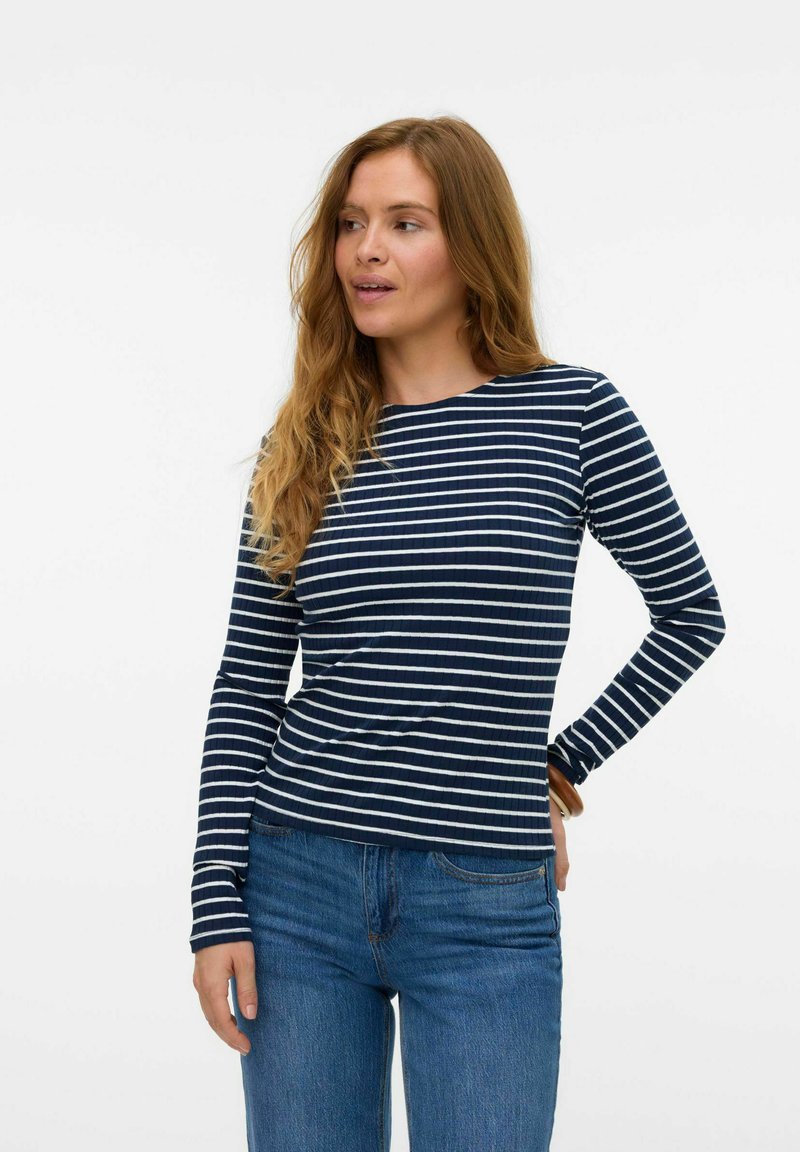 Långärmad marinblå randig topp i ribbat tyg, med vita ränder, rund halsringning och åtsittande design, matchad med blå denimjeans.