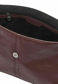 Brązowa skórzana saszetka o gładkiej fakturze, z zapięciem na srebrny zatrzask oraz czarną materiałową podszewką z kieszenią na zamek w środku.