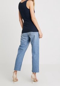 Marineblauw tanktop gecombineerd met lichtblauwe hooggerelateerde jeans. De jeans hebben een rafelige zoom. Crème kleurige hakken maken de look compleet.