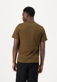 Camiseta marrón de manga corta hecha de algodón, con cuello redondo y un diseño sencillo sin logotipos ni patrones visibles.