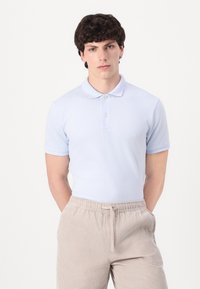 Polo de manga corta color azul claro con cuello y tapeta de tres botones, combinado con pantalones de pana color beige con cinturilla elástica.