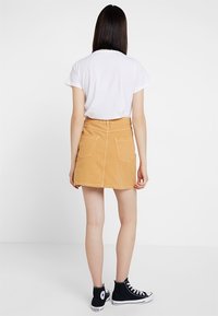 Minifalda de mezclilla en naranja claro, con corte recto, dos bolsillos traseros y detalles cosidos, combinada con una camiseta blanca y zapatillas negras.