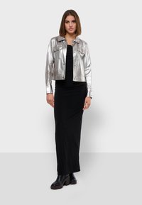 Veste cropped argentée métallique avec une fermeture à boutons, deux poches poitrine, associée à une robe noire ajustée et des bottes à plateforme noires.
