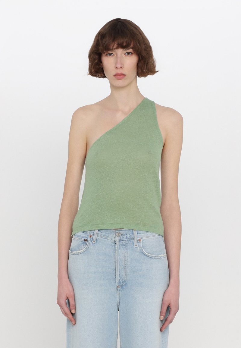 Asymmetrisk grön topp av texturerad tyg, med design för en axel. Matchas med ljusblå högmidjade jeans.