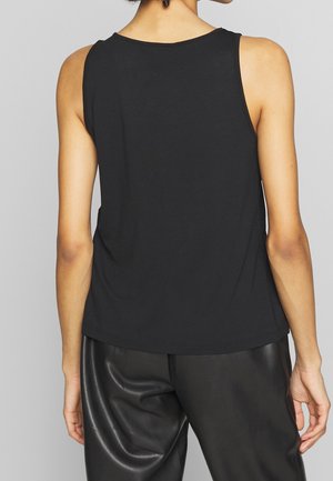 Osoba ubrana w czarny top bez rękawów i czarne skórzane spodnie, pokazana od tyłu na jednolitym szarym tle.